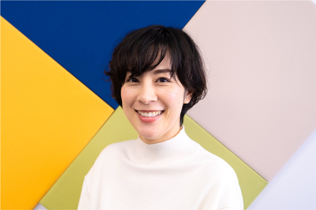 カラフルな背景の前に立つ、笑顔の女性の写真